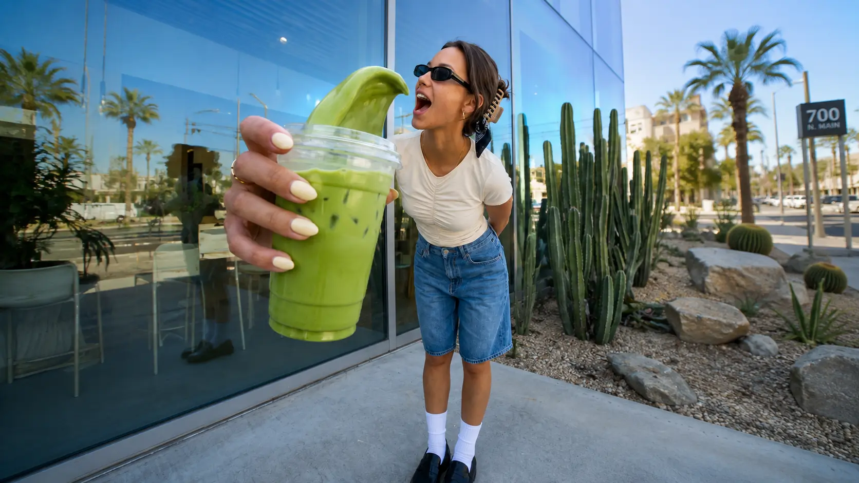 Woman presenting a green drink outside a cafe before background blur.