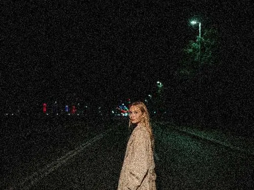 A grainy low-light portrait on a dark street before denoising.